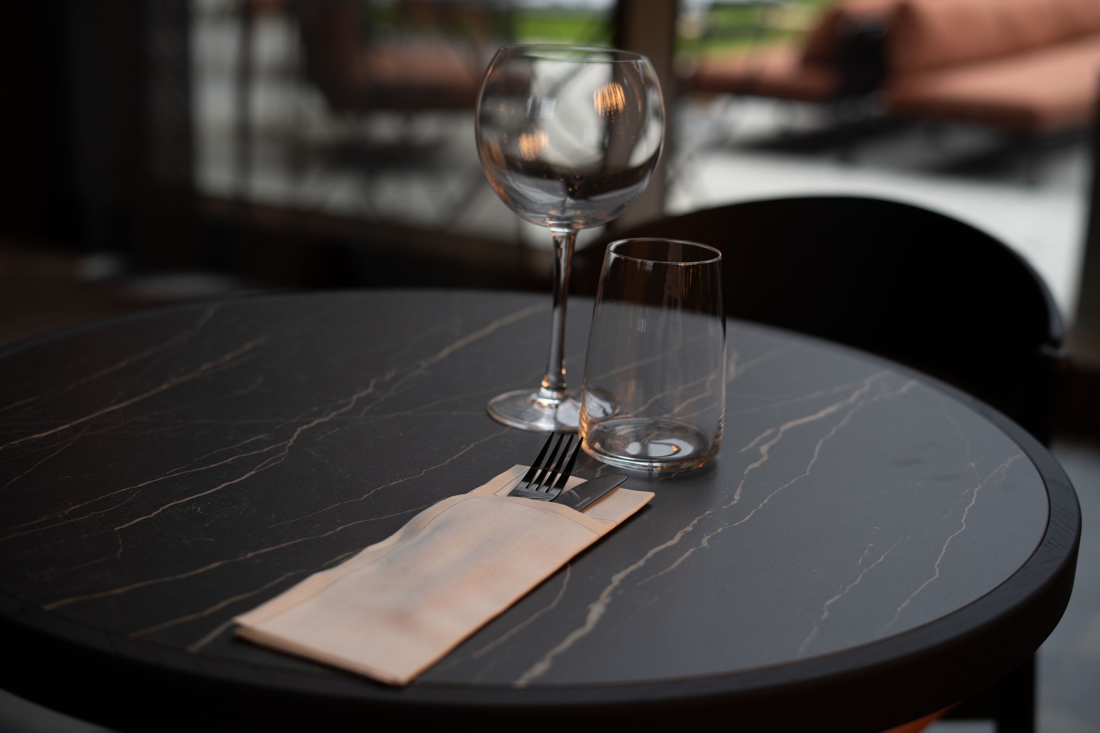 Een ronde tafel met een donker marmeren blad, een wijnglas, een waterglas en een gevouwen servet.