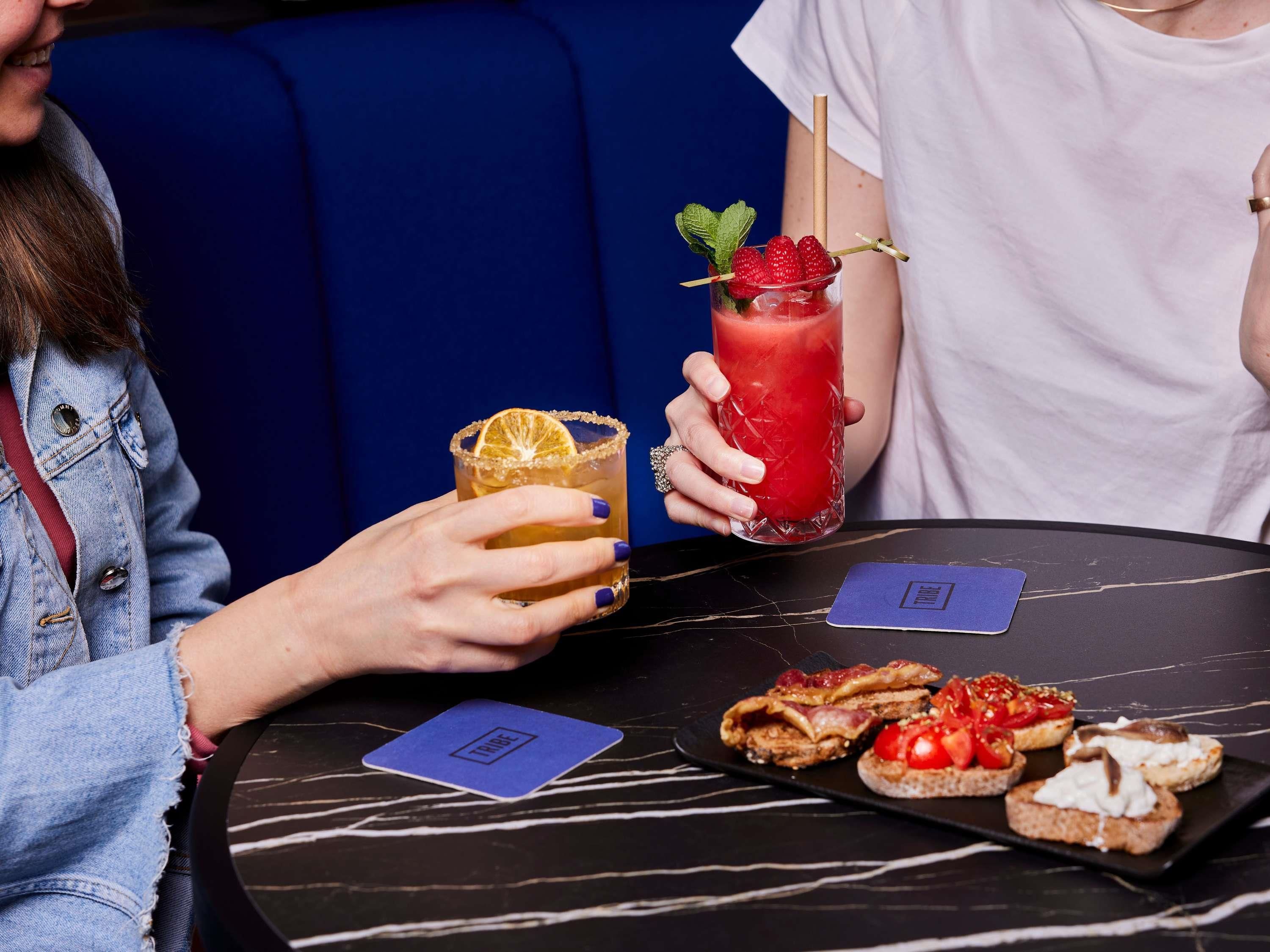 Deux personnes sont assises à une table, devant des boissons et de la nourriture.