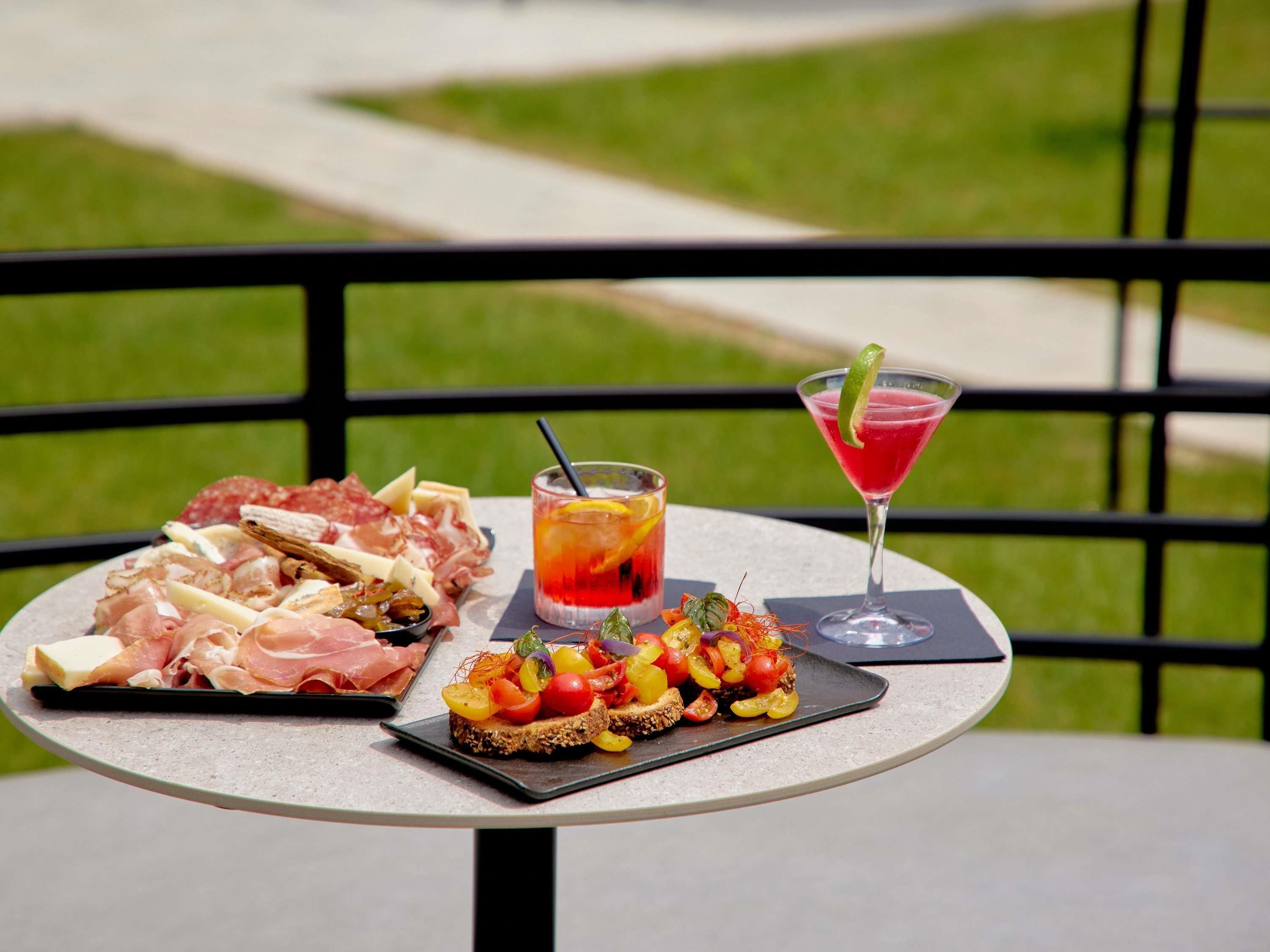 Una mesa con una tabla de embutidos, una copa de martini y un cóctel con una rodaja de lima.