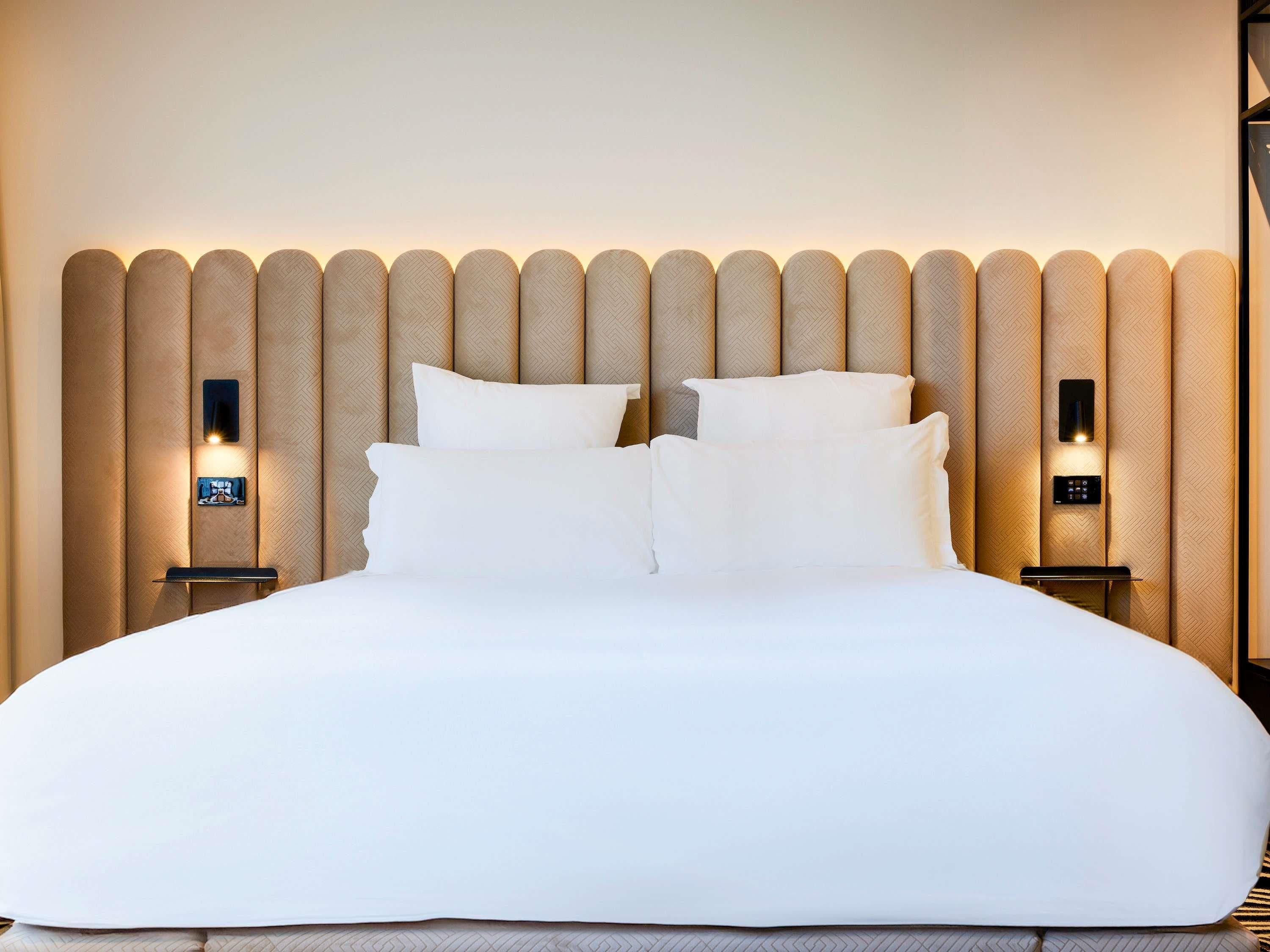 Una cama bien hecha con cabecera de paneles verticales e iluminación integrada.