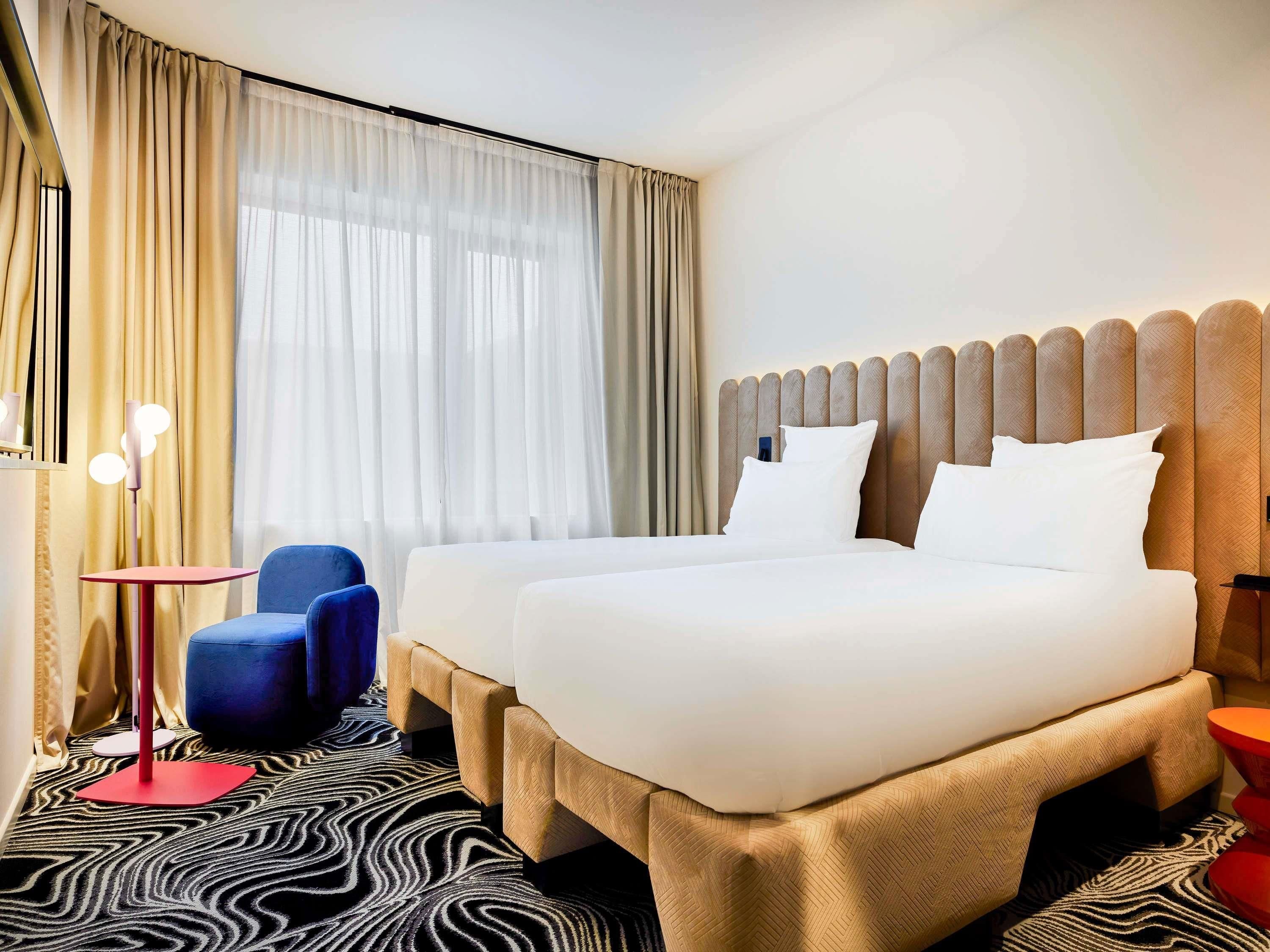 Une chambre d’hôtel avec un lit, deux tables de chevet, une chaise et une moquette à motifs.