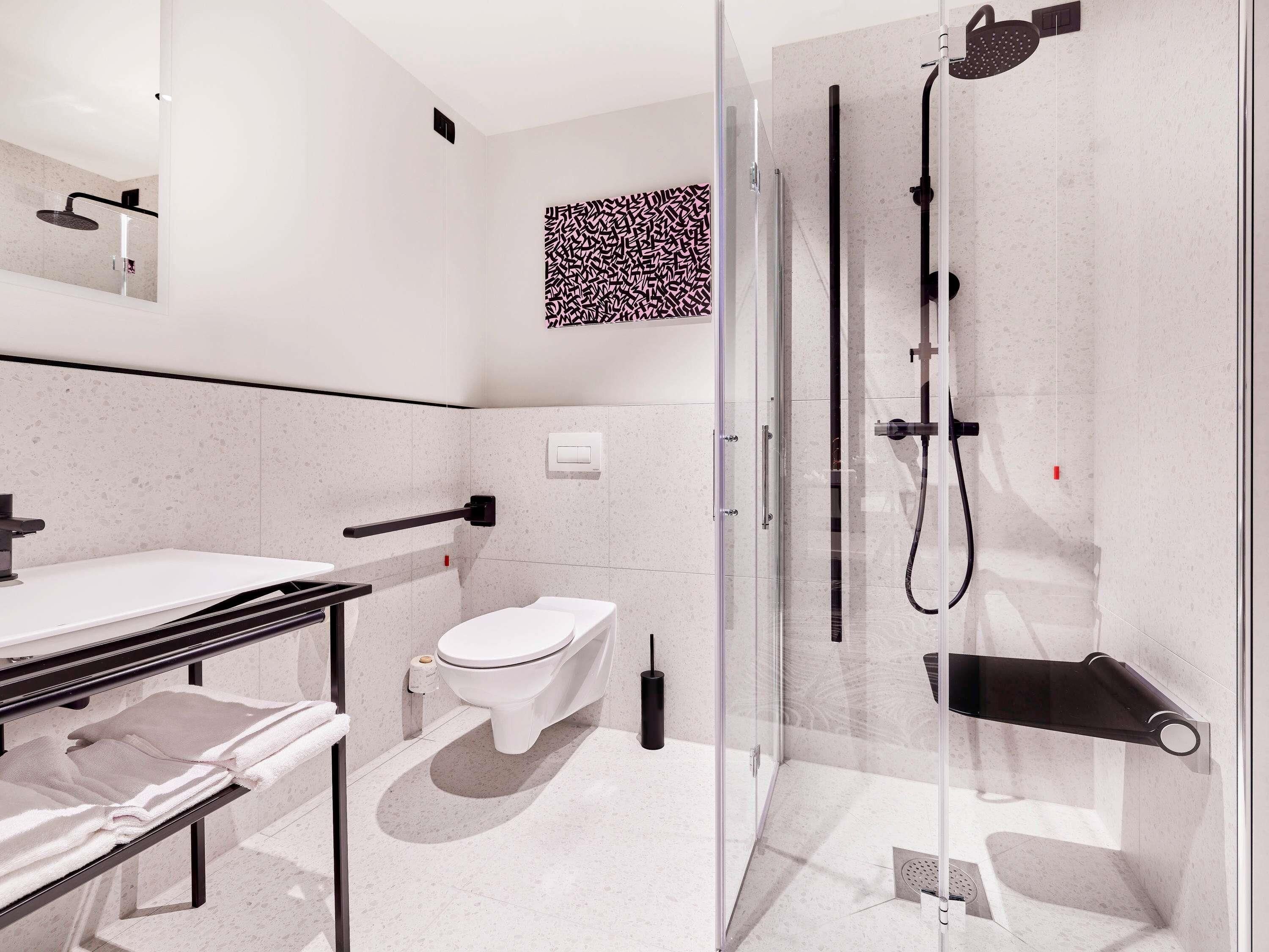 A modern bathroom with a glass-enclosed shower, a white toilet, and a vanity with a towel rack.