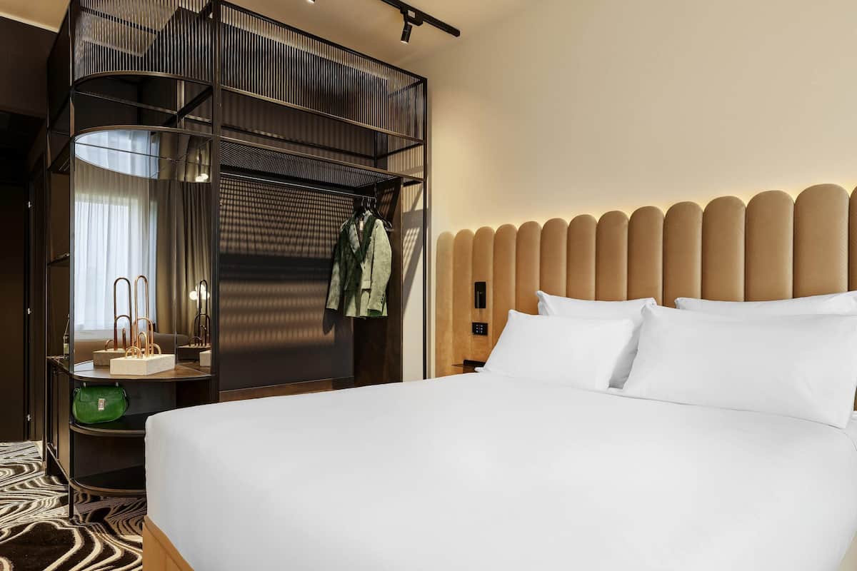 A hotel room with a bed, a mirror, a wardrobe, and a nightstand.