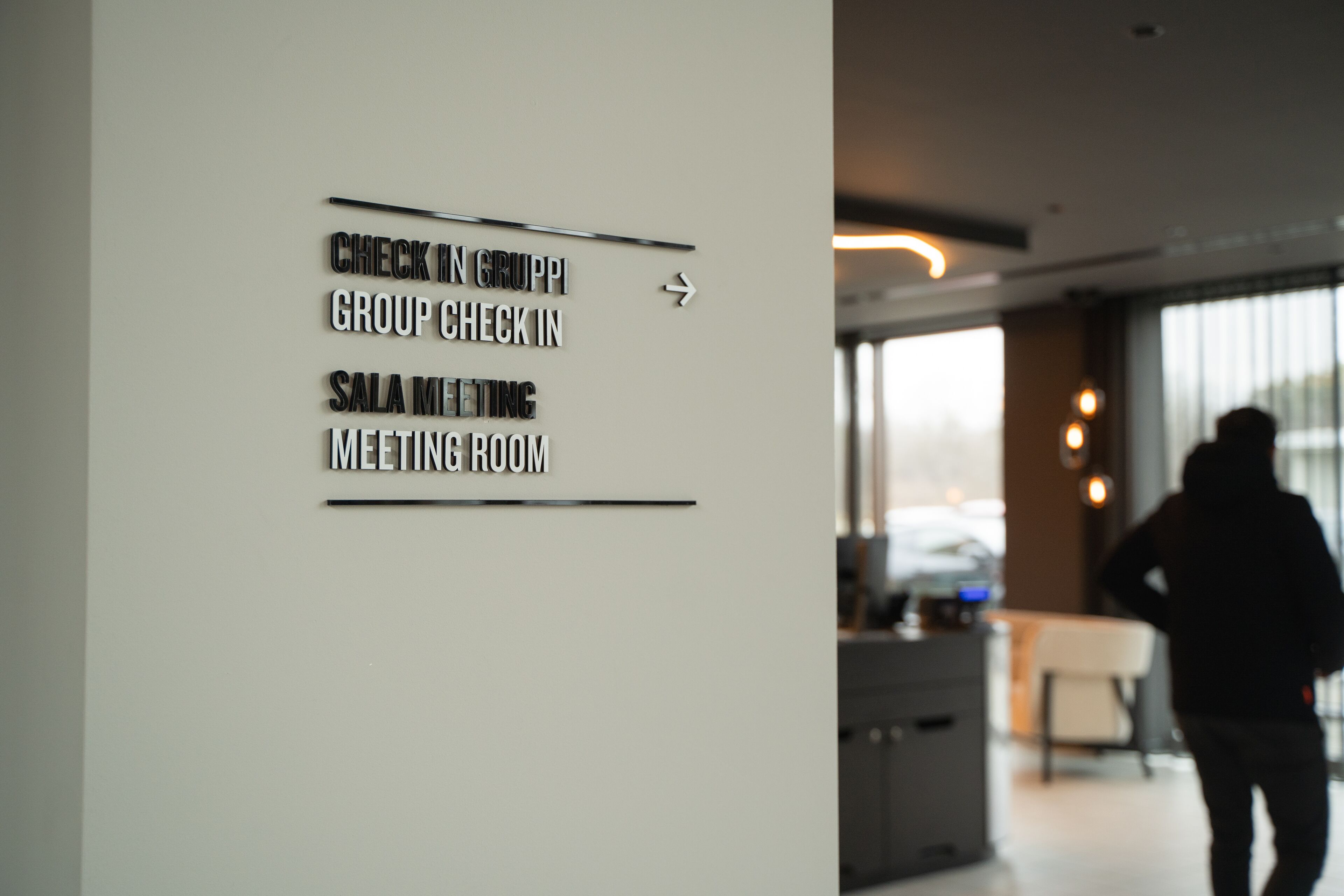A wall with directional signs for 'Check In Group', 'Group Check In', 'Sala Meeting', and 'Meeting Room'.