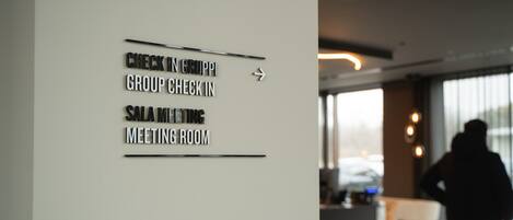 A wall with directional signs for 'Check In Group', 'Group Check In', 'Sala Meeting', and 'Meeting Room'.