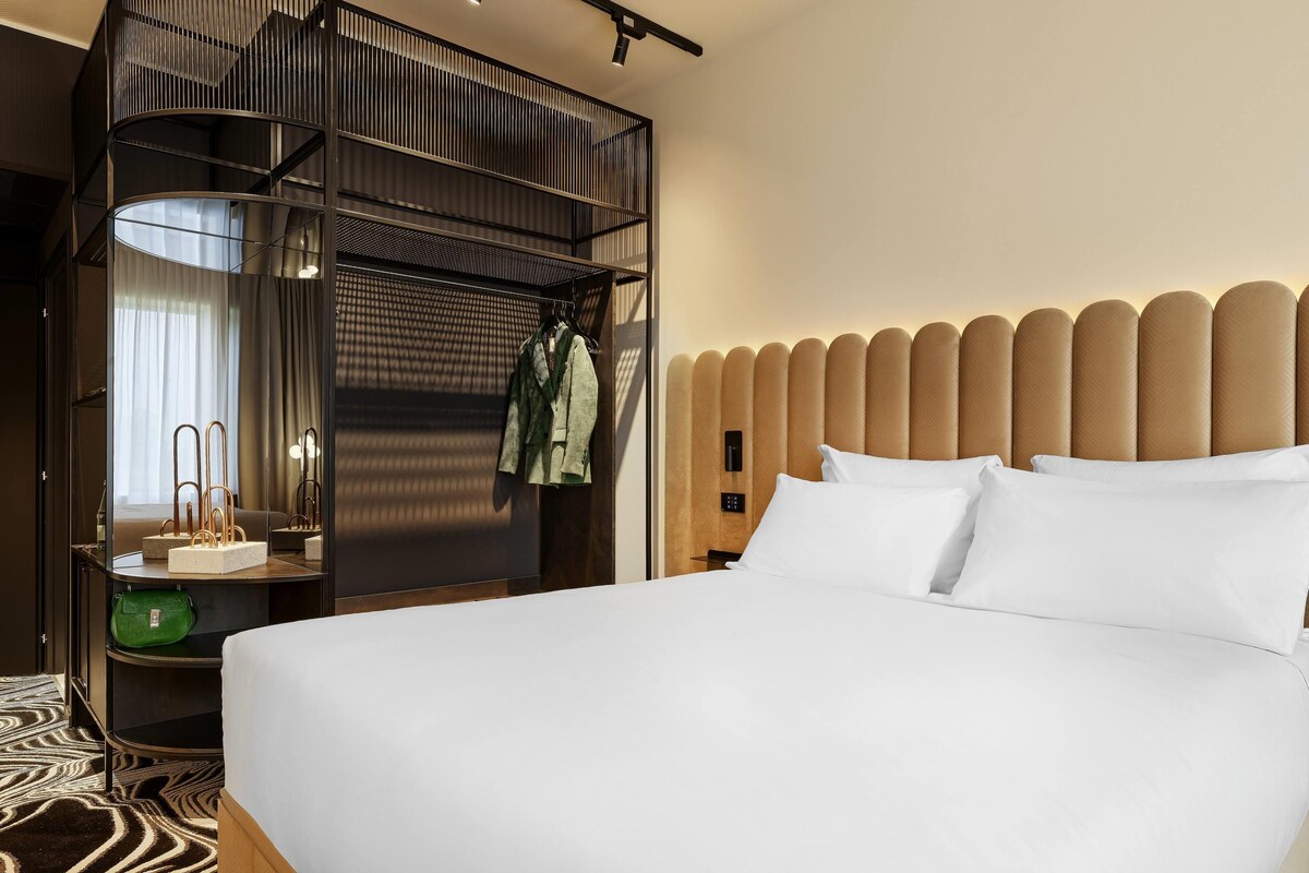 A hotel room with a bed, a mirror, a wardrobe, and a nightstand.