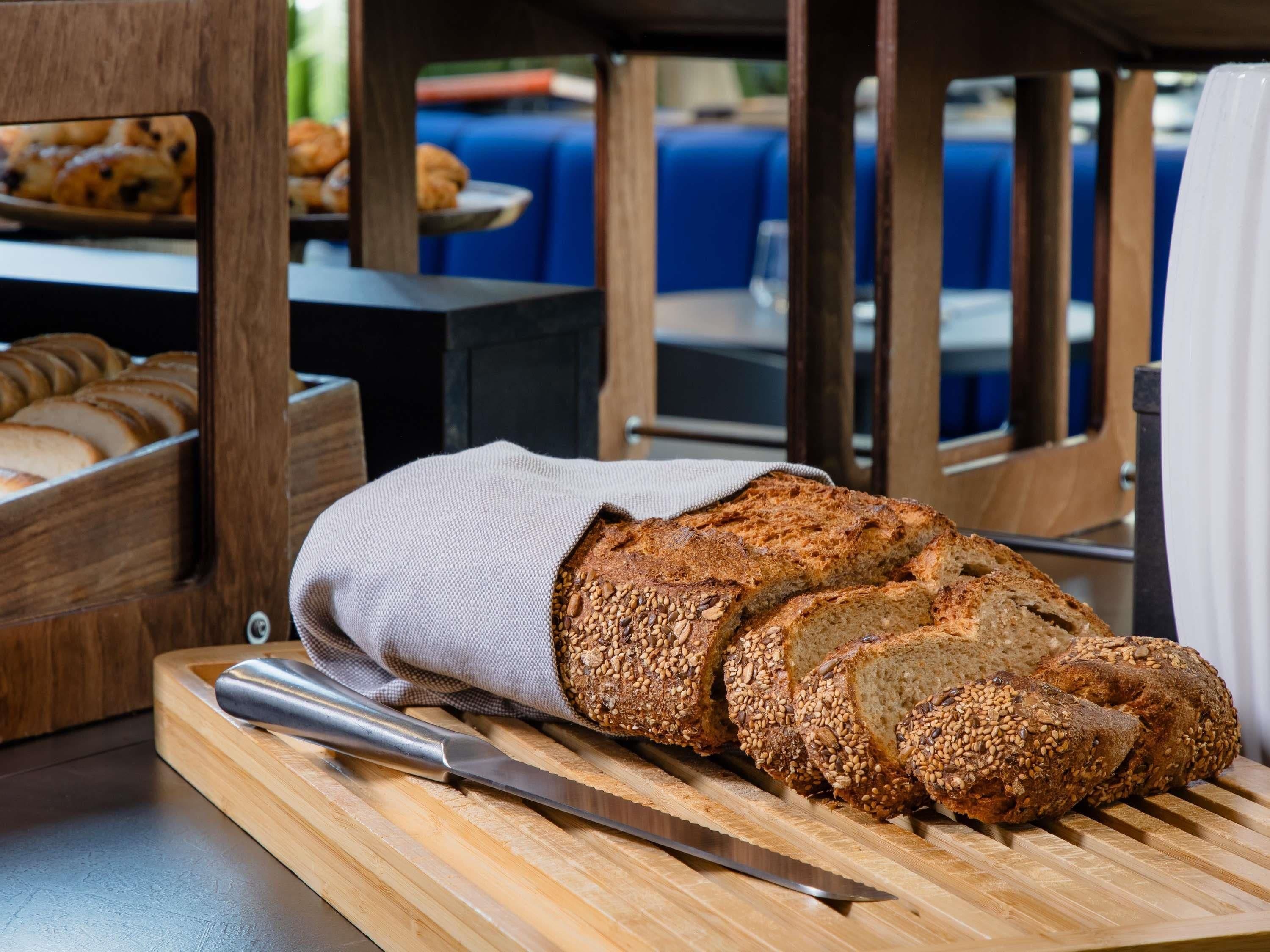 Una hogaza de pan con semillas sobre una tabla de madera con un cuchillo, en una cocina.