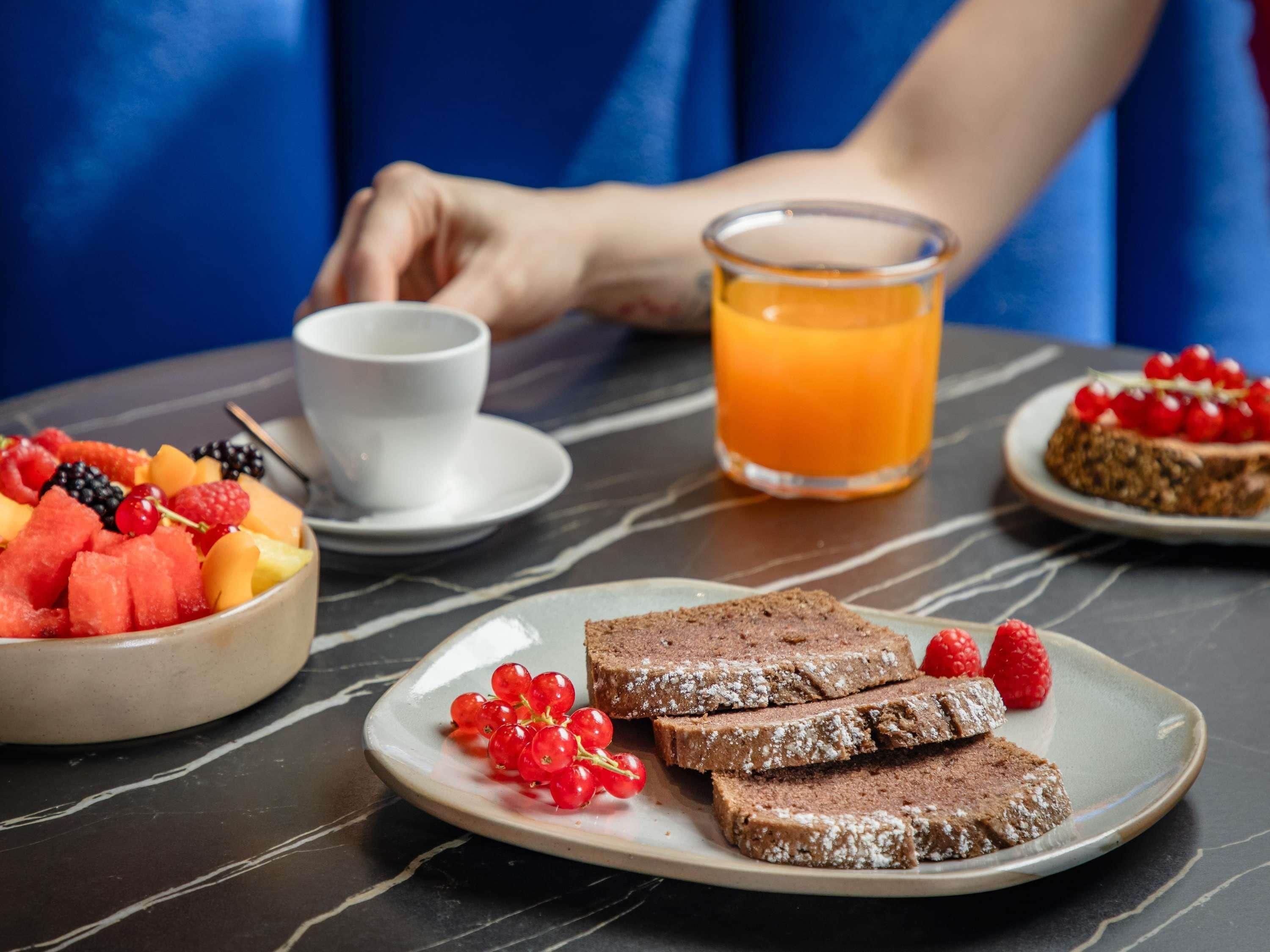 A breakfast setting with a plate of sliced bread, a bowl of mixed fruit, a glass of orange juice, and a cup on a table.