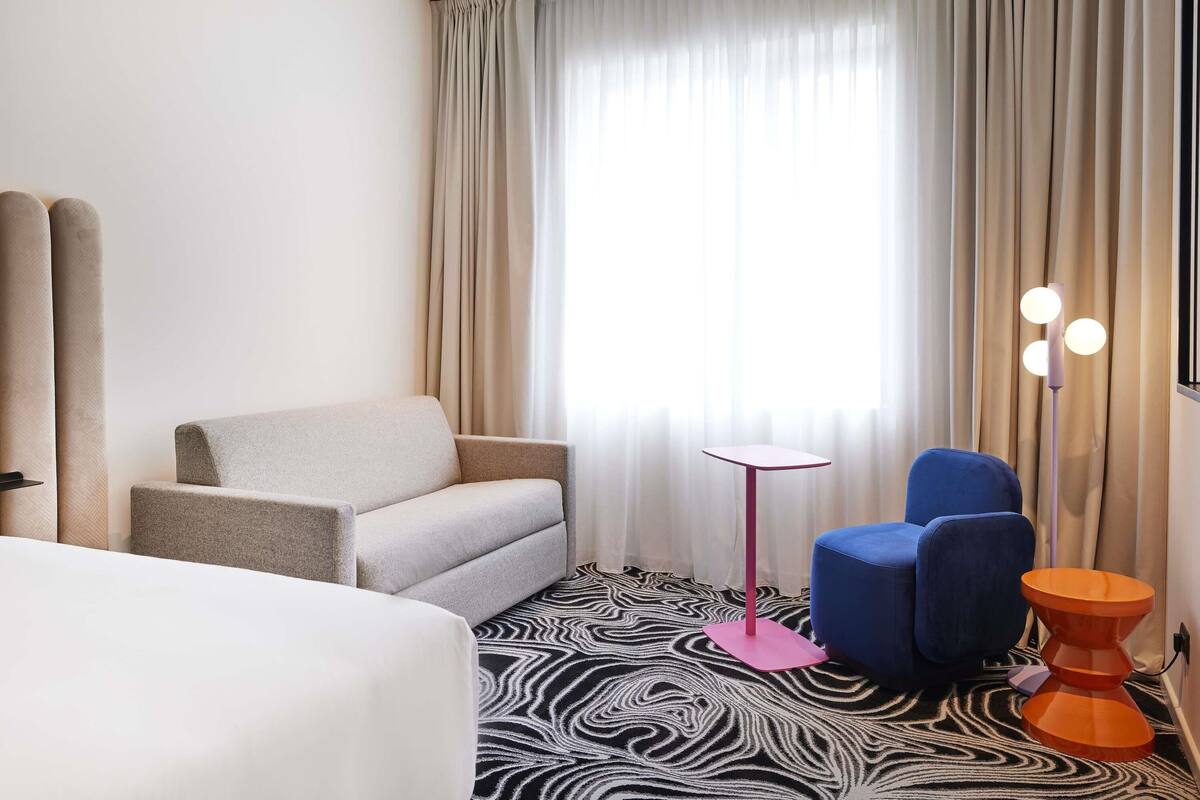 A hotel room with a bed, a sofa, a small table, a blue chair, and a zebra-patterned rug.