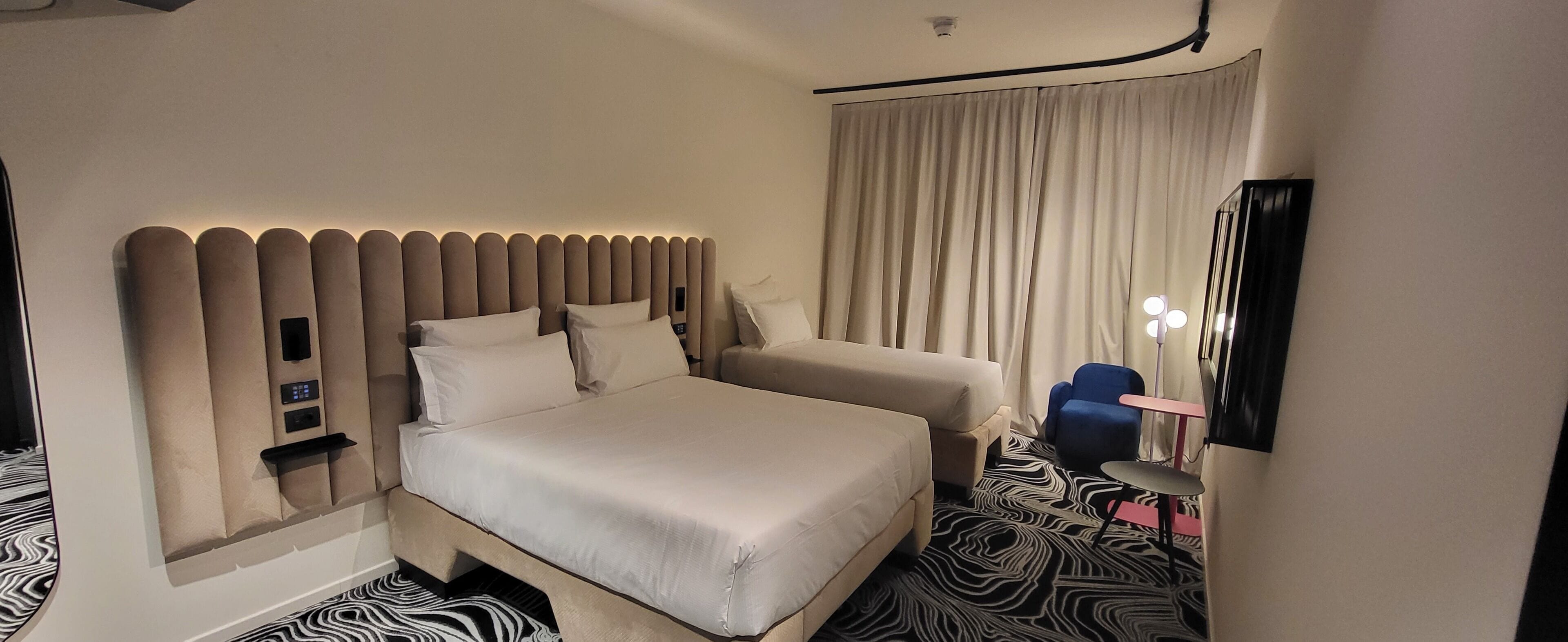 Una camera d'albergo con un letto grande, un divano, un tavolino, uno specchio e un tappeto a motivi zebrati.