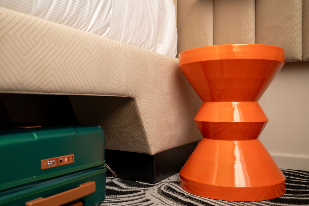 A room with a bed, a patterned wall, a green suitcase, and an orange object.