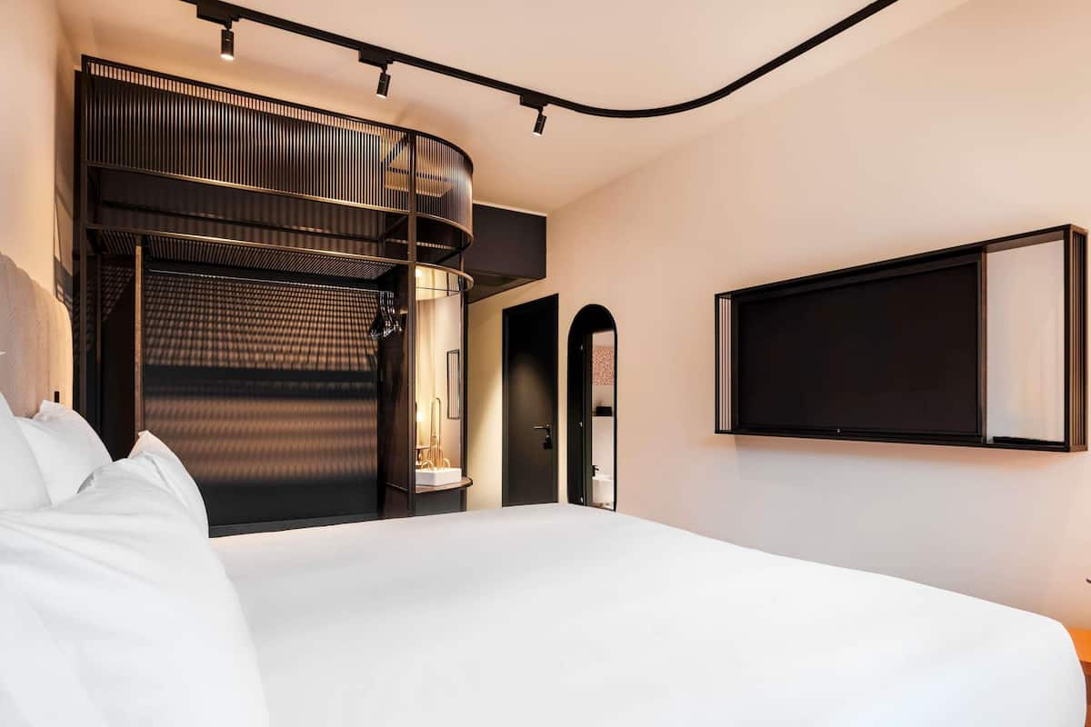 A modern hotel room with a large bed, a curved ceiling, and a built-in seating area with a view of the city.
