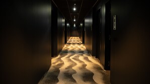 A hallway with a patterned carpet, dark walls, and a series of doors on either side. - Tribe Milano Malpensa (Vizzola Ticino)
