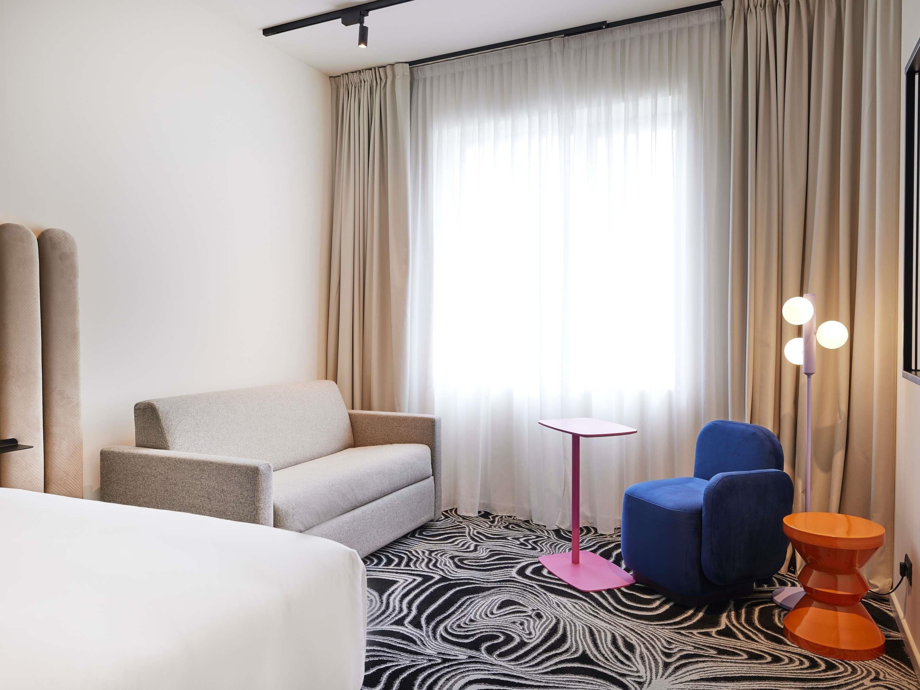 Una habitación de hotel con cama, sofá, una mesita, una silla azul y un alfombra con estampado de cebra.