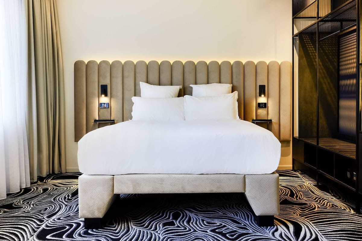 A hotel room with a large bed, two bedside tables, a headboard with built-in lighting, and a patterned carpet.