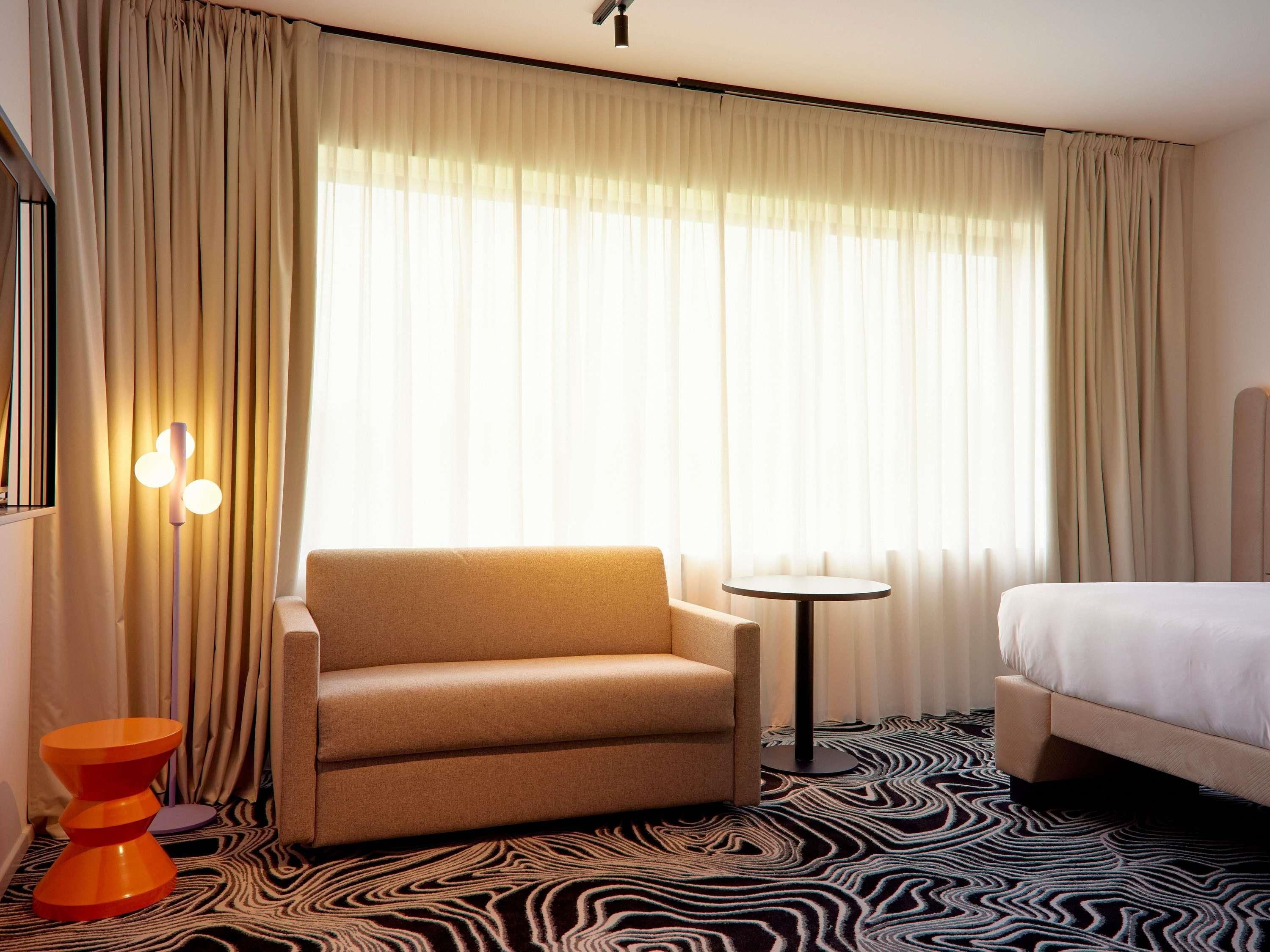 Une chambre d’hôtel avec un lit, une chaise, une petite table et une lampe.