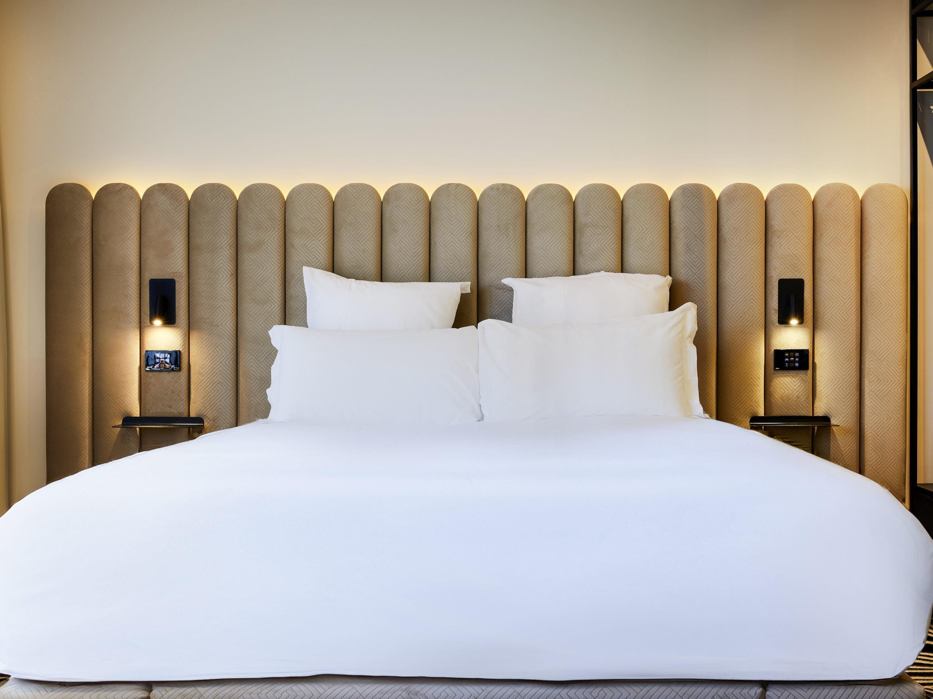 Une chambre d’hôtel avec un grand lit, deux tables de chevet et un panneau de commande fixé au mur.