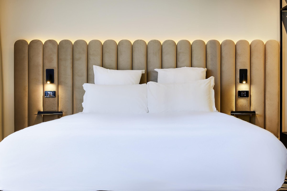 Une chambre dâhĂŽtel avec un grand lit, deux tables de chevet et un panneau de commande fixĂ© au mur.