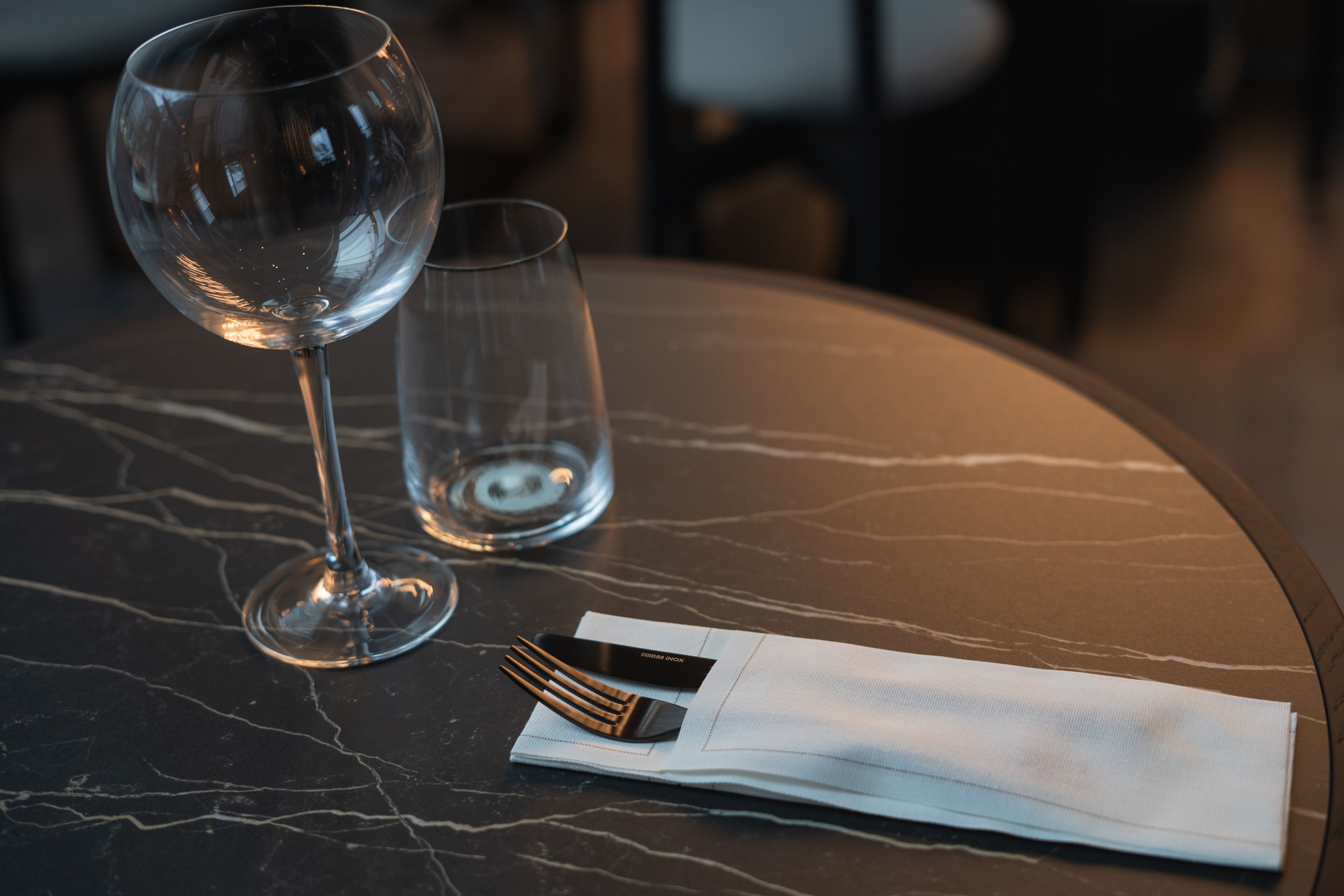 Una mesa con una copa de vino, un vaso más pequeño, una servilleta doblada y un cuchillo sobre una superficie de mármol.