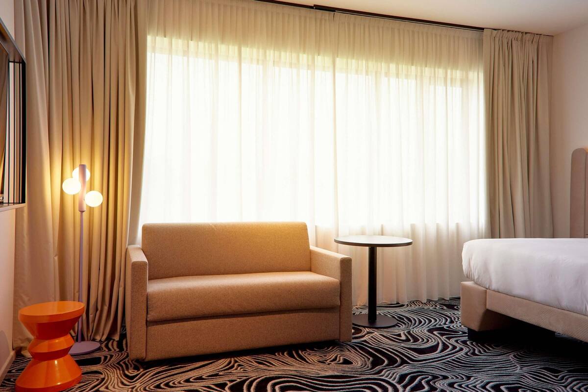 A hotel room with a bed, a chair, a small table, and a lamp.