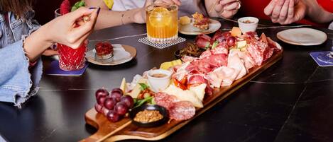 A table with a charcuterie board, a glass of beer, and a person holding a drink.