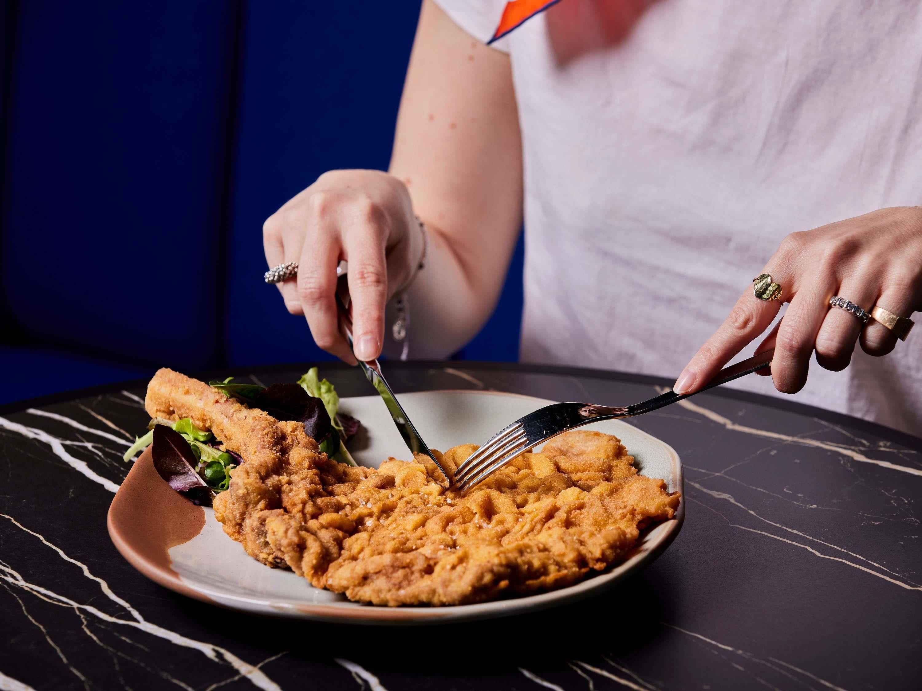 Una persona cortando un plato con guarnición usando un tenedor y un cuchillo.