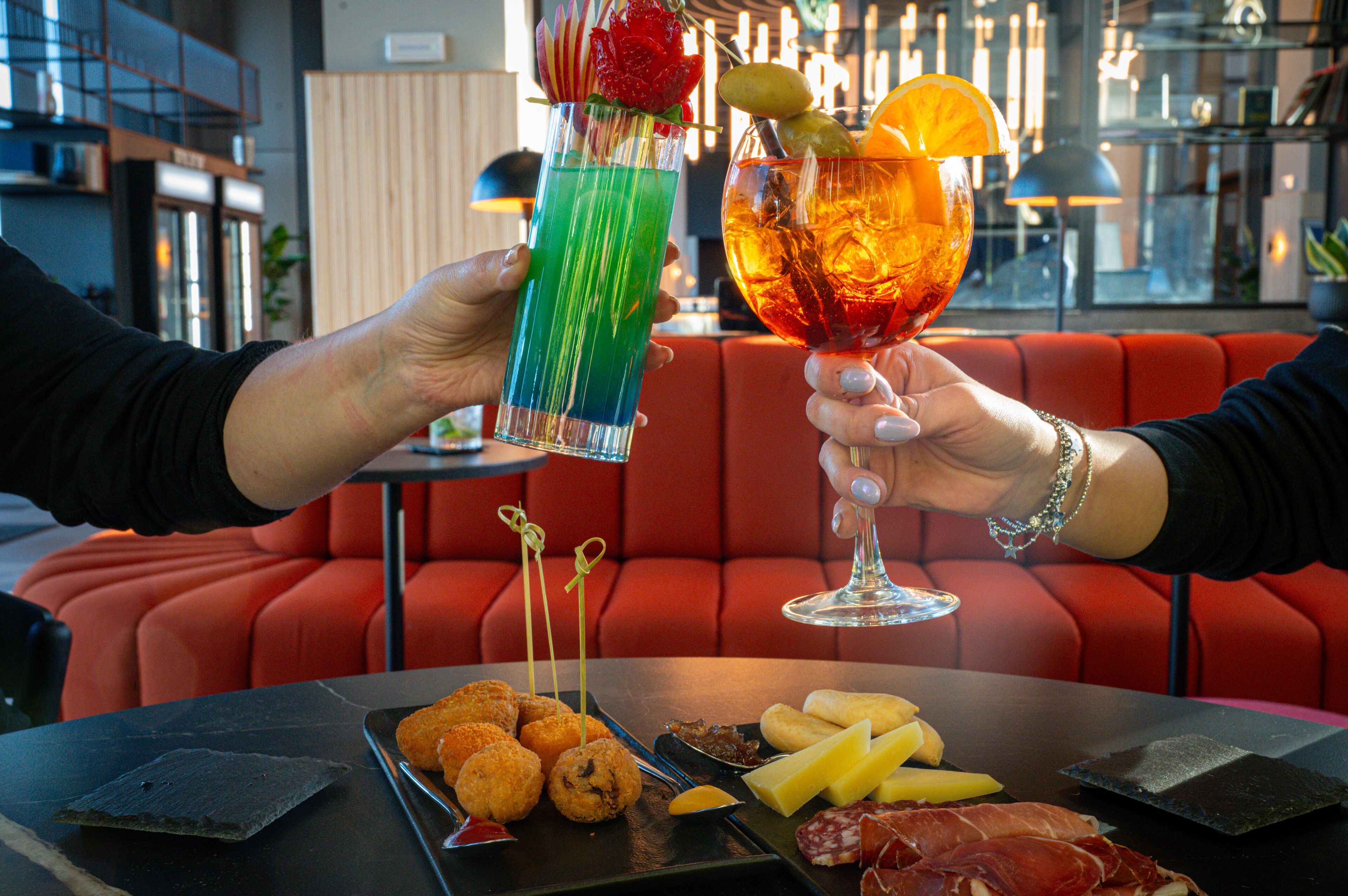 Eine Person hält einen Cocktail mit Limettenspalte und Erdbeere, daneben ein Cocktail mit Orangenscheibe und Minze.