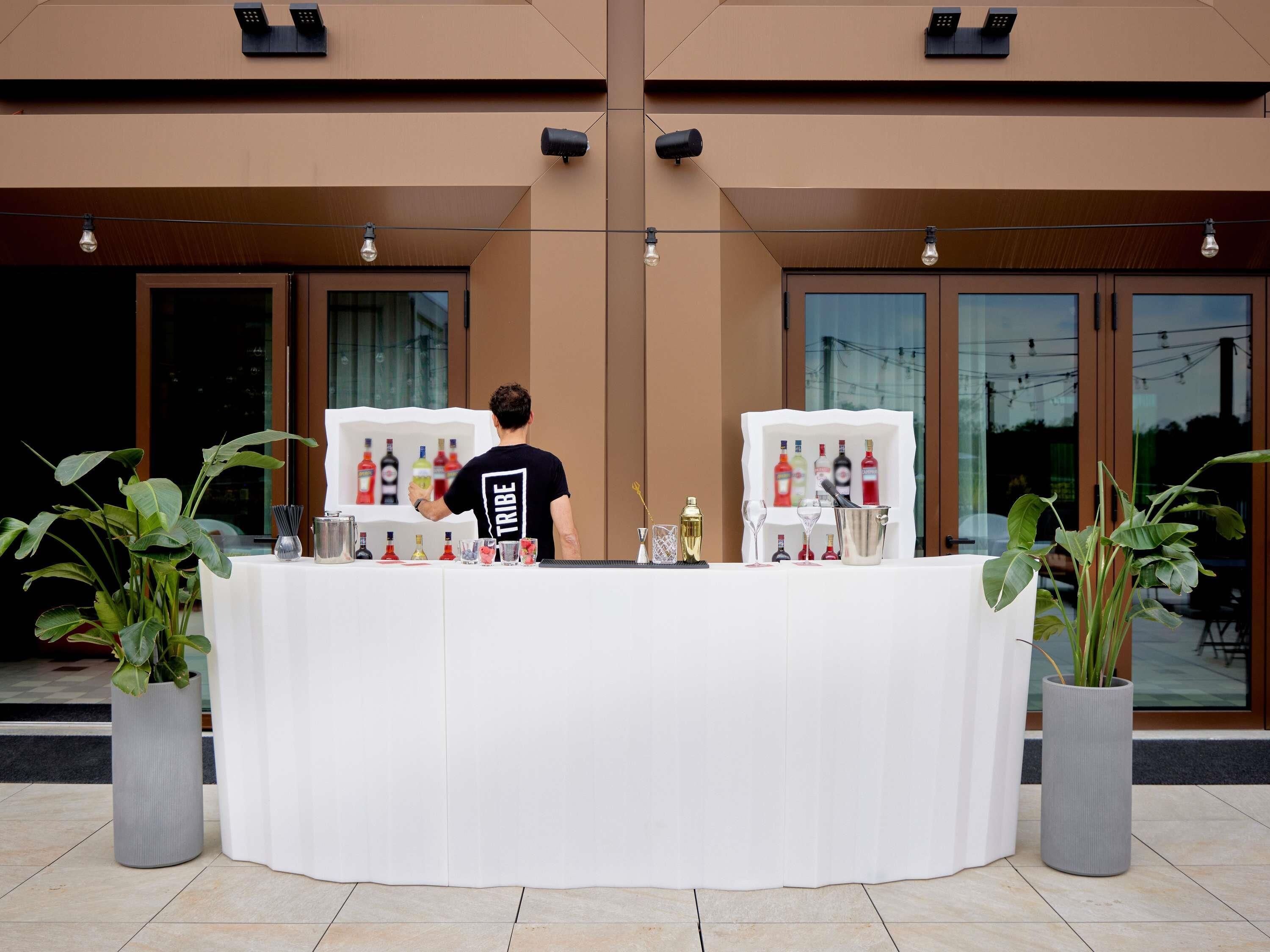Zona de bar con un bartender, una barra blanca y una exhibición de botellas.