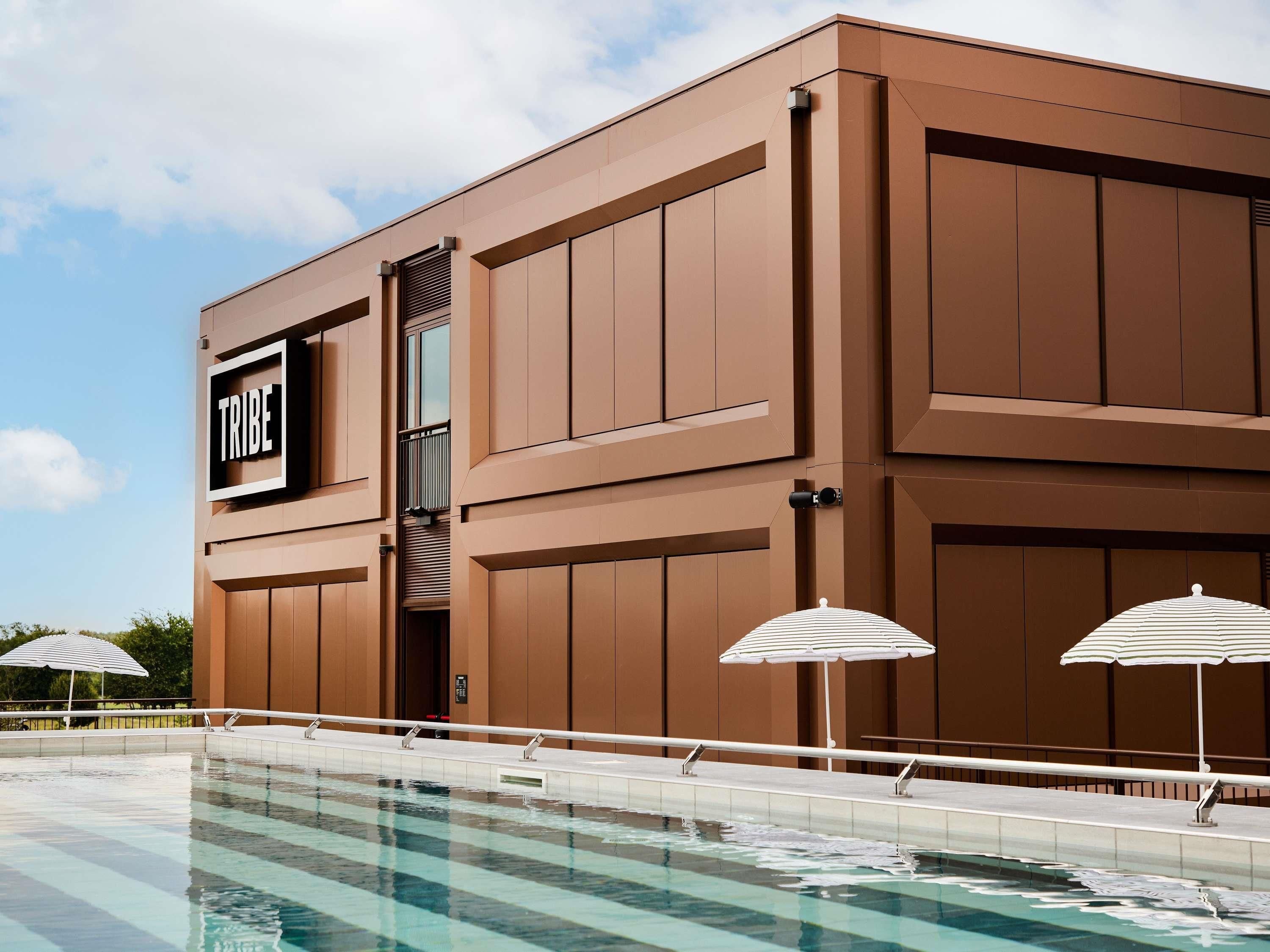 A modern building with a sign reading 'TRIBE' and a pool area with umbrellas.