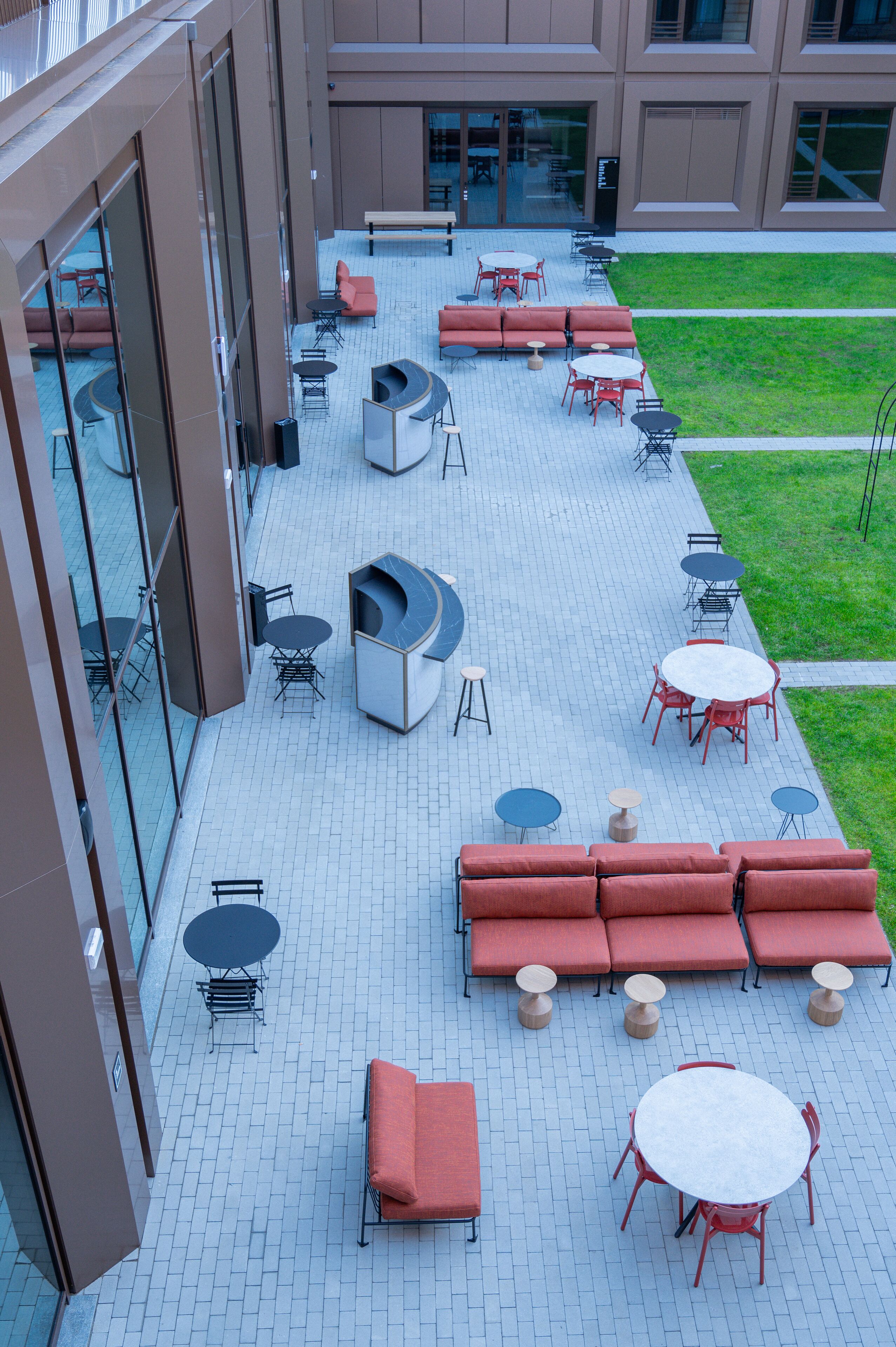Une terrasse sur le toit avec des espaces de détente en plein air, comprenant des canapés et des tables, ainsi qu’un espace clos par des parois de verre, équipé de chaises.