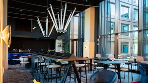 A modern lounge area with a bar, seating arrangements, and a contemporary light fixture. - Tribe Milano Malpensa (Vizzola Ticino)