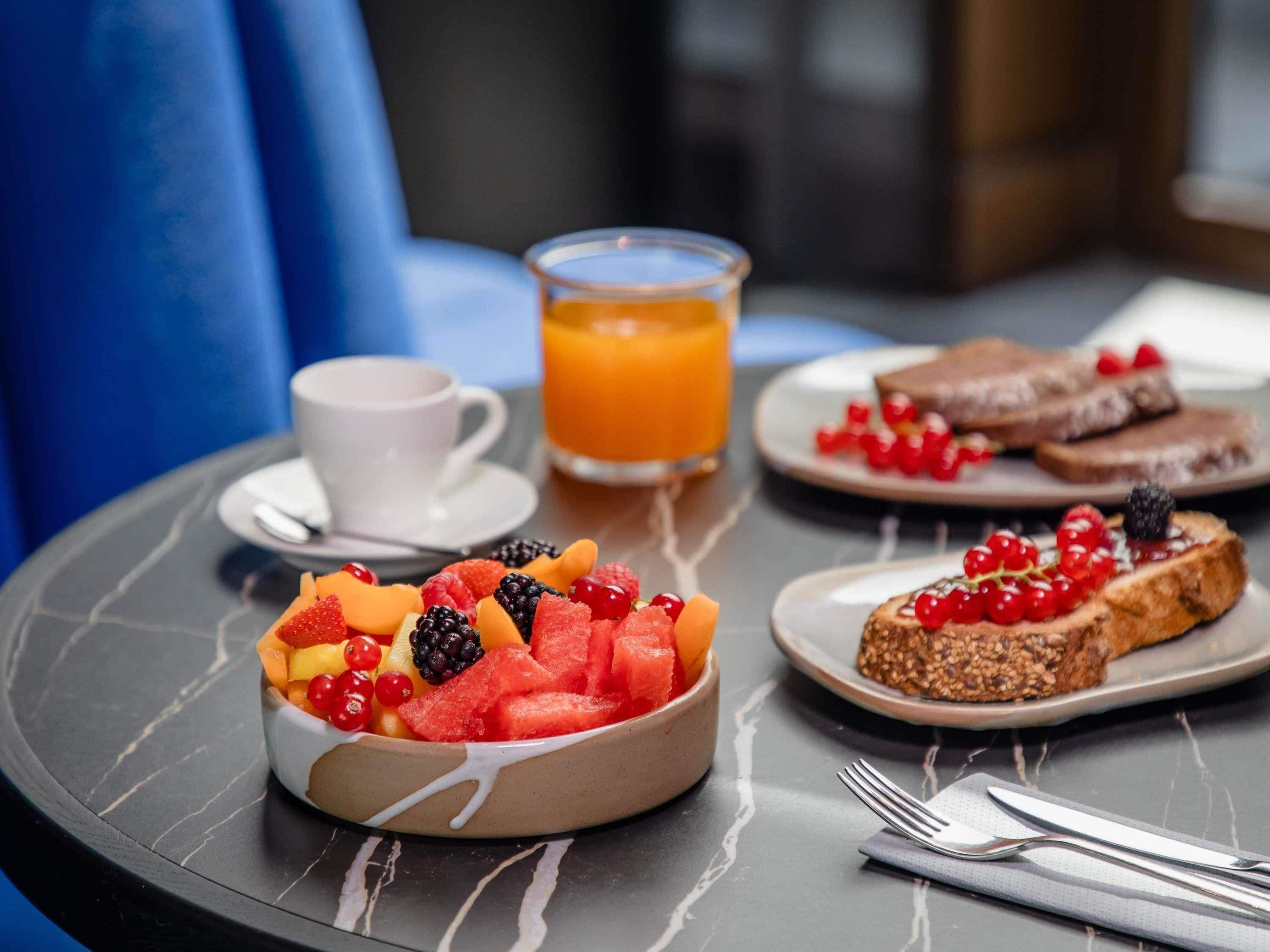 A breakfast setting with a fruit bowl, toast with berries, a cup of coffee, and a glass of orange juice on a table.
