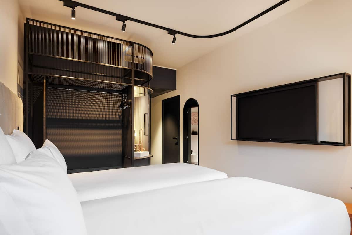 Une chambre dâhĂŽtel moderne avec un grand lit, un meuble mural aux lignes courbes et un tĂ©lĂ©viseur fixĂ© au mur.