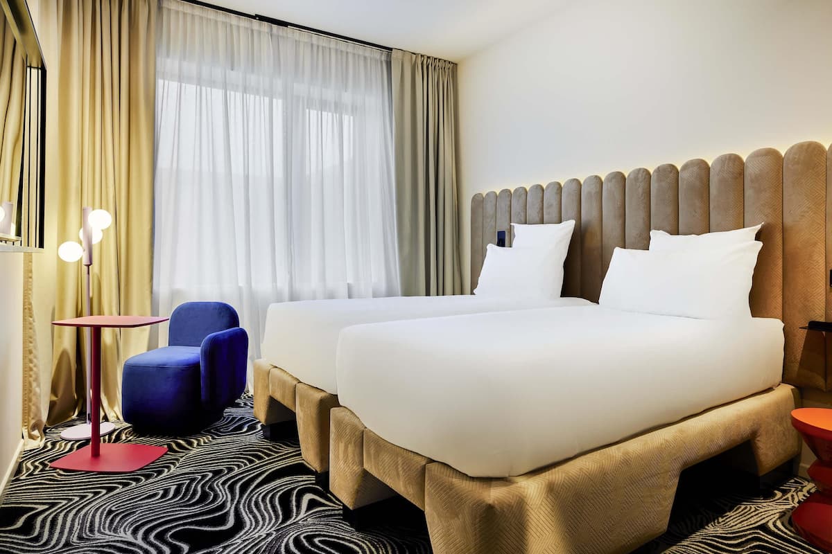 Une chambre dâhĂŽtel avec deux lits, une chaise bleue, une table rouge et un tapis Ă motifs.