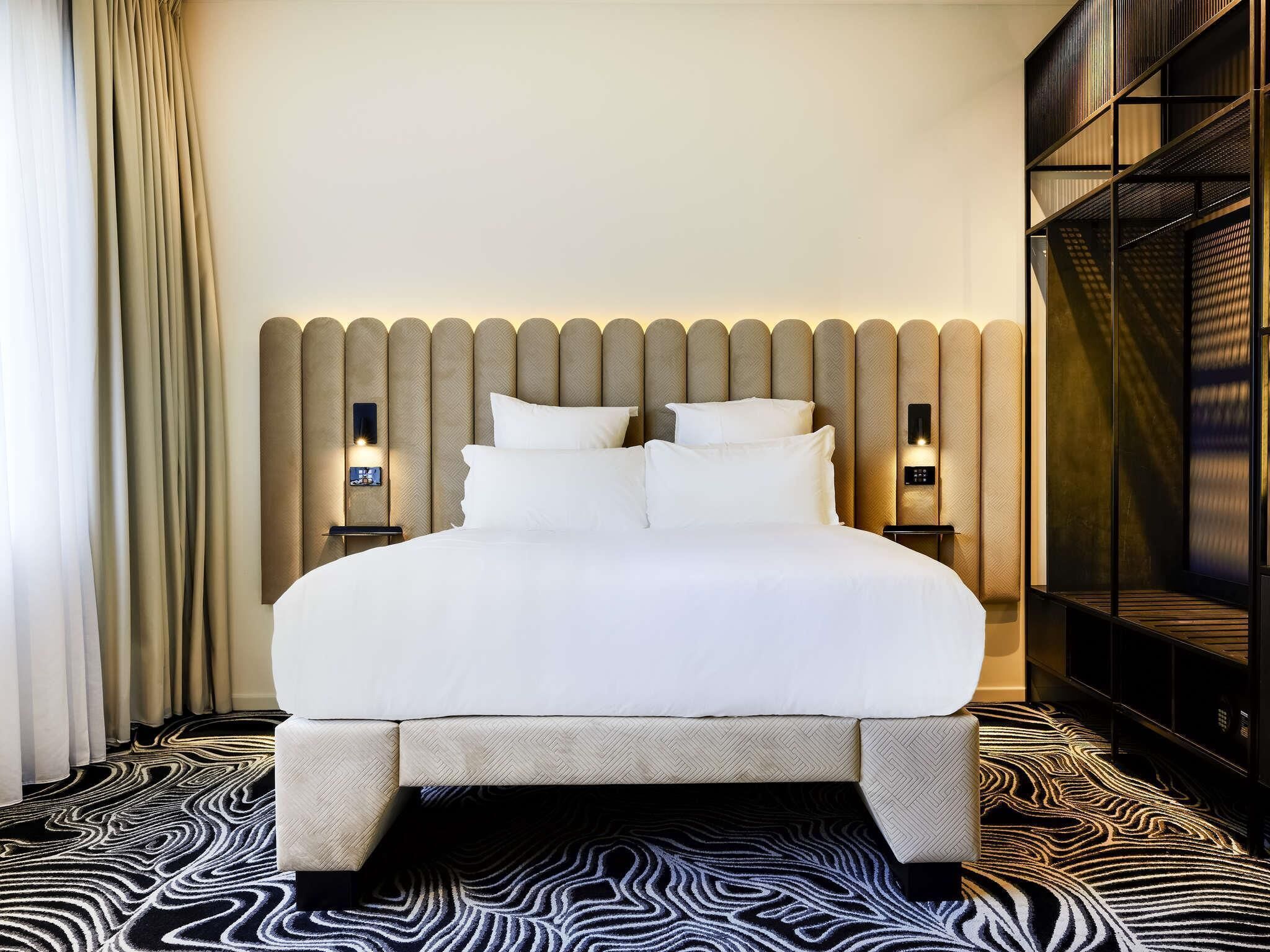 A hotel room with a large bed, two bedside tables, a headboard with built-in lighting, and a patterned carpet.
