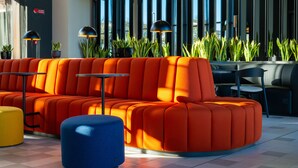 Un área de descanso moderna con un sofá naranja intenso, un puf azul y mesas negras.