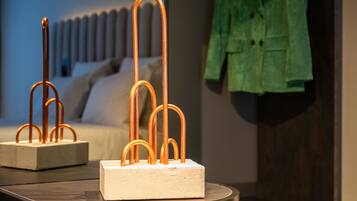 Una habitación moderna con una cama, una mesa y una escultura de luz geométrica, además de una chaqueta verde colgada en la pared.