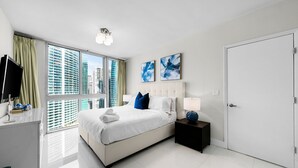 A modern hotel room with a large bed, a bedside table, a TV, and a view of tall buildings. - ICON W BRICKELL LUXURIOUS OCEAN VIEW 2BR/2BA #3002 (Miami)