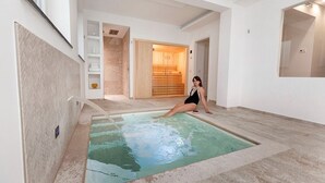 A spacious indoor swimming pool with a wooden door in the background, a tiled floor, and a white wall with a shelf.