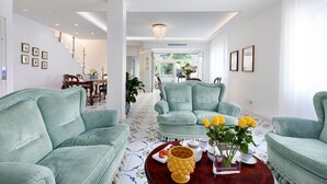 A spacious living room with teal sofas, a coffee table with yellow flowers, and a chandelier.