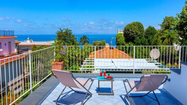 A balcony with two lounge chairs, a small table, and a potted plant.