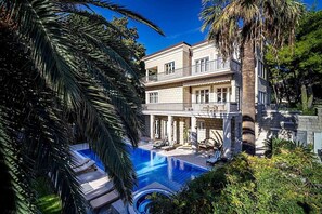 Una casa de dos pisos con piscina, mobiliario exterior y un balcón.