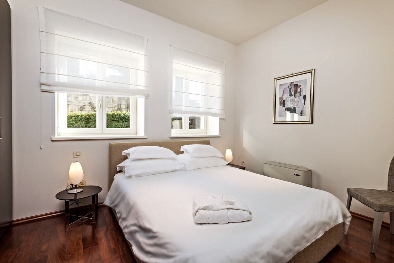 A neatly arranged bedroom with a bed, two bedside tables, a chair, and a radiator.