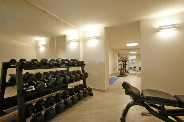 A gym with a mirrored wall, a bench, and a rack of dumbbells.