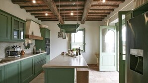 Une cuisine avec des meubles de couleur verte, un grand îlot central et un plafond en bois rustique.