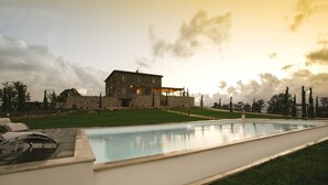 Une maison en pierre avec une piscine, entourée d’une pelouse et d’arbres.