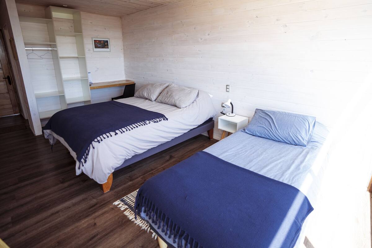 A bedroom with two beds, wooden flooring, a wardrobe, and a nightstand with a lamp.