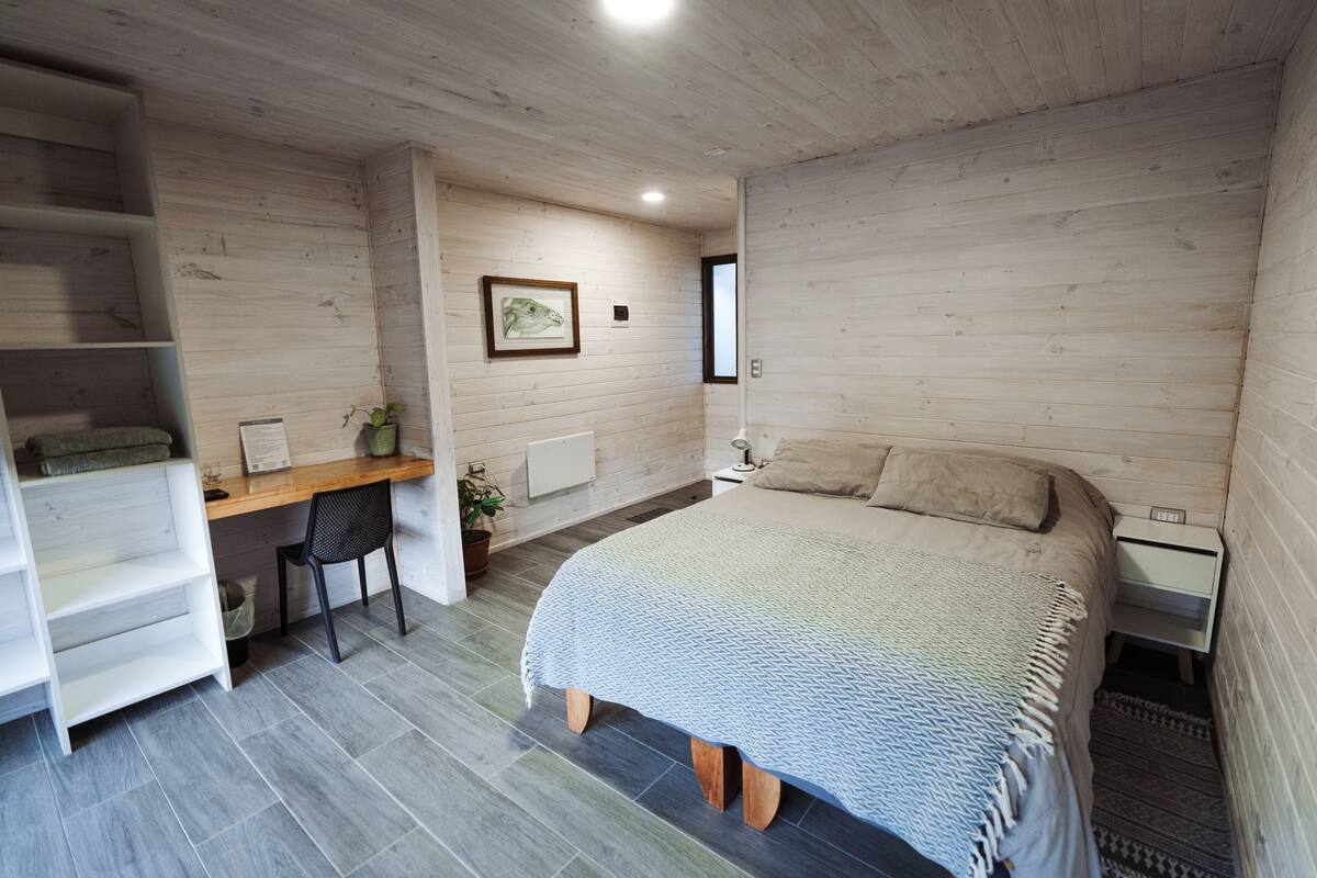 A bedroom with a bed, a desk, a chair, and a shelf unit.
