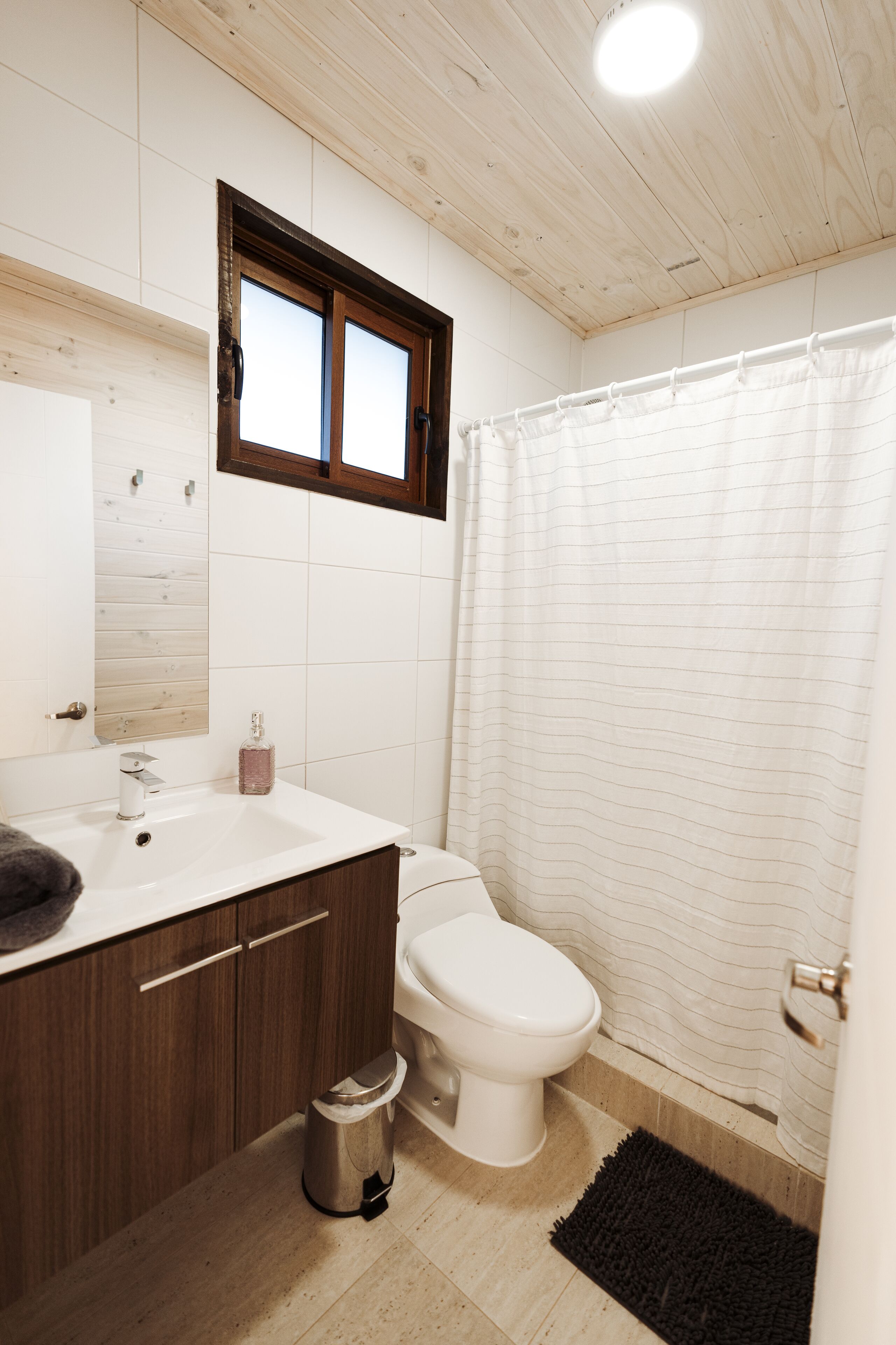 A bathroom with a wooden ceiling, a white sink with a mirror, a toilet, and a shower curtain.