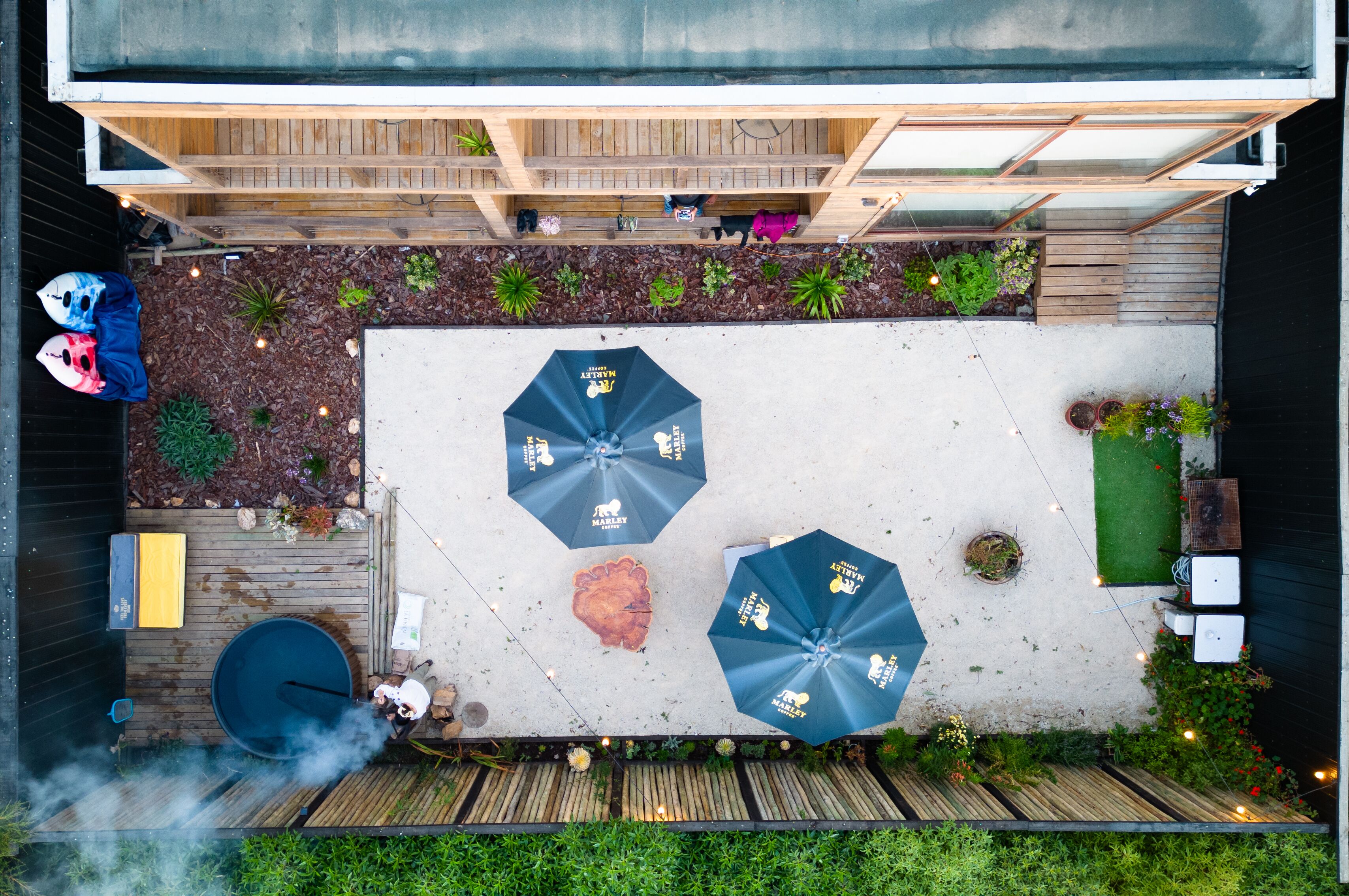 An outdoor patio with wooden flooring, two umbrellas, and a seating area with cushions.